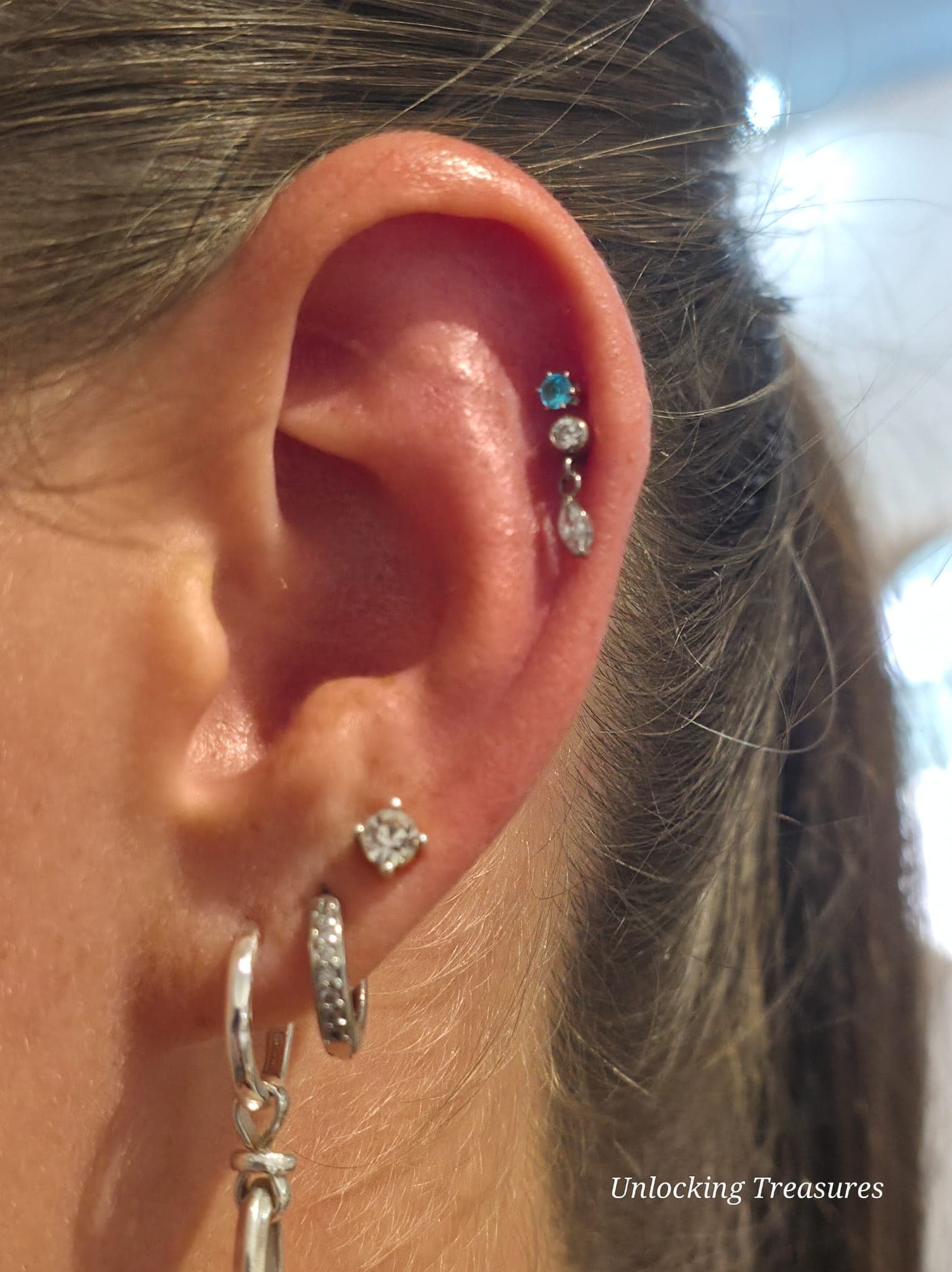 Close-up of a helix piercing with a turquoise stud and stacked lobe piercings